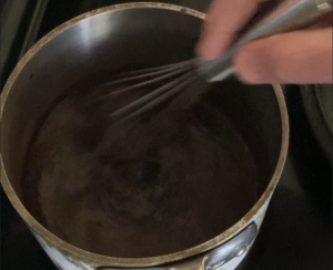 Stirring sugar cree chocolate syrup in a saucepan.